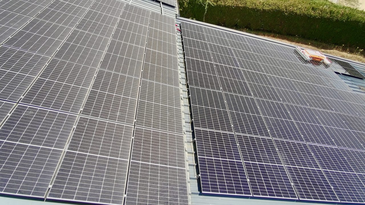 Grande toiture photovoltaïque : la moitié gauche est encrassée, la moitié droite a été nettoyée par le robot Optisun, visible en haut à droite